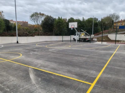Prikaz iscrtanih linija za košarku i rukomet na asfaltnoj podlozi uz koš za košarku.
