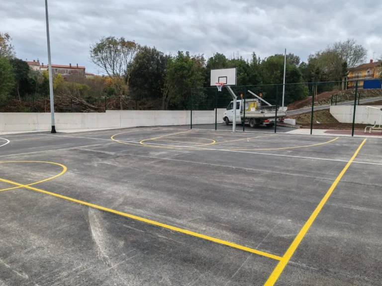 Prikaz iscrtanih linija za košarku i rukomet na asfaltnoj podlozi uz koš za košarku.