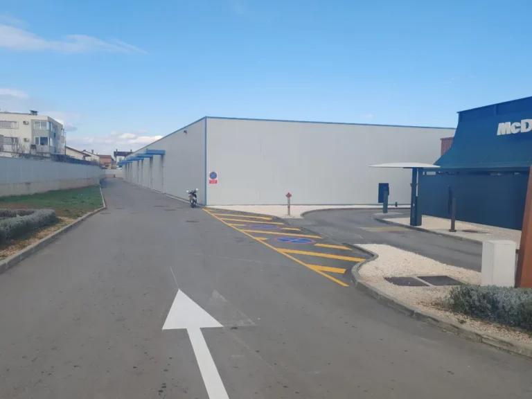 Bijela strelica za usmjeravanje prometa iscrtana na asfaltu prilazne ceste.