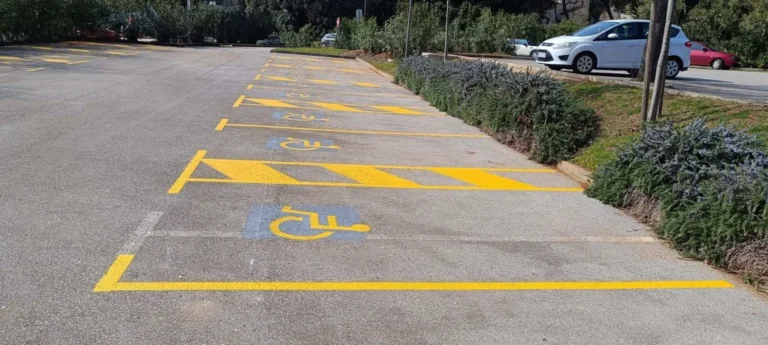 Niz označenih parkirnih mjesta za invalide uz žuta polja za usmjeravanje prometa.