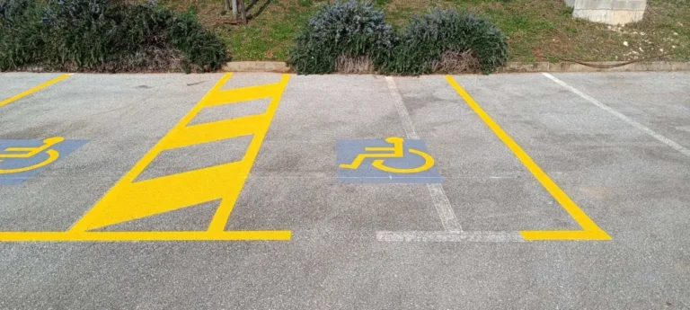 Iscrtana žuta parkirna mjesta za osobe s invaliditetom s plavim piktogramima.