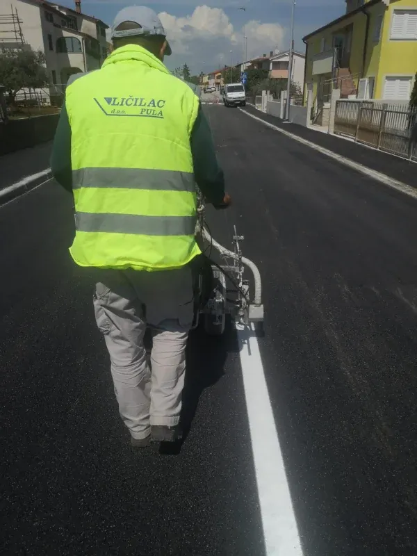 Djelatnik u reflektirajućem prsluku s natpisom LIČILAC d.o.o. Pula iscrtava rubnu liniju na kolniku