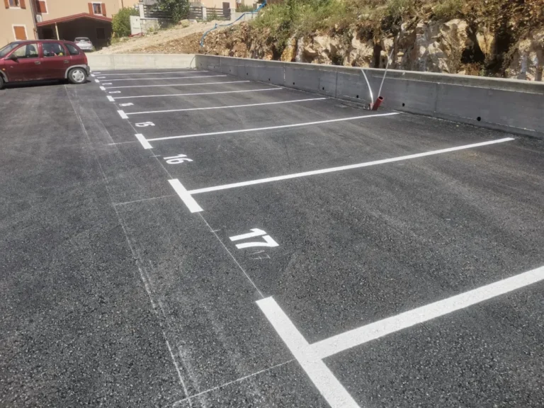 Niz označenih parkirnih mjesta s brojevima uz betonski potporni zid u Plomin Luci.