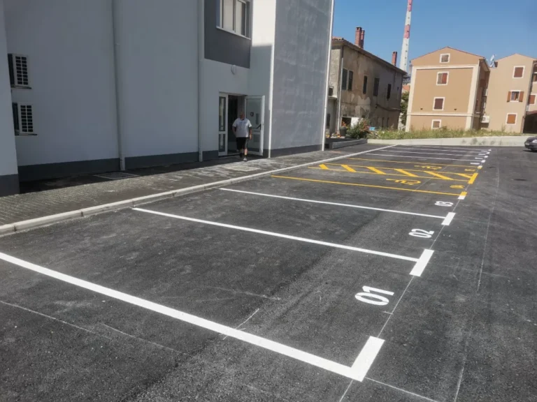 Iscrtana i numerirana parkirališna mjesta bijelom bojom ispred stambene zgrade.