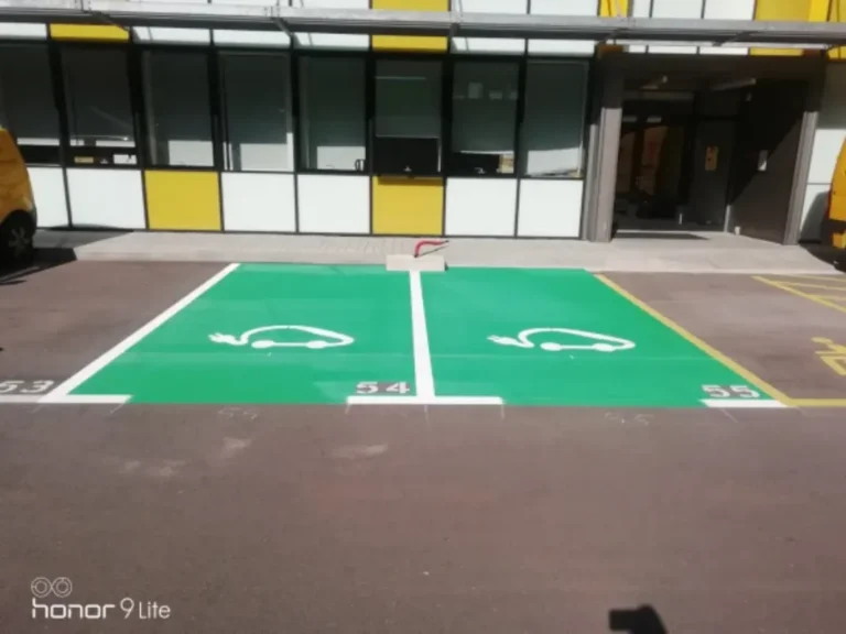 Jasno označena zelena parkirna mjesta za punjenje električnih vozila uz poslovnu zgradu.