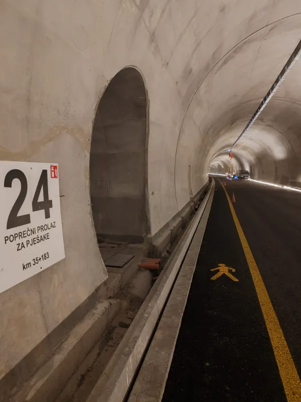 Oznaka za poprečni prolaz za pješake i iscrtani žuti simbol pješaka na asfaltu unutar tunela.