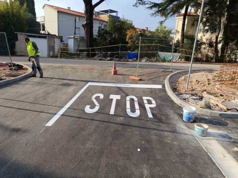Veliki bijeli natpis STOP i zaustavna linija iscrtani na asfaltu.