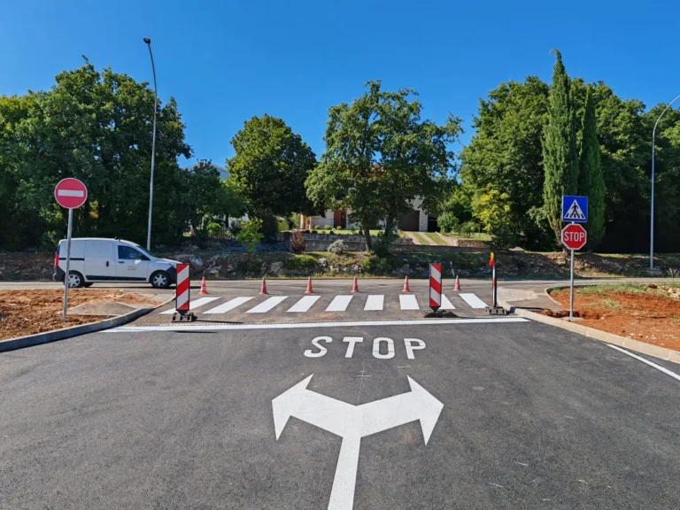 Svježe iscrtan pješački prijelaz i oznaka STOP na asfaltu uz postavljene vertikalne prometne znakove na ulazu u benzinsku postaju.