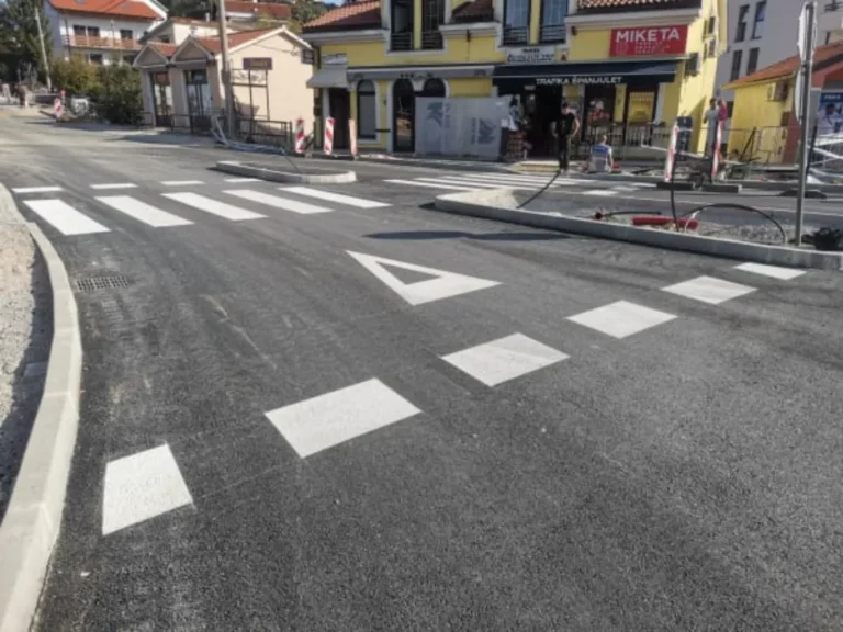 Iscrtani pješački prijelazi i bijele oznake za usmjeravanje prometa oko prometnih otoka.