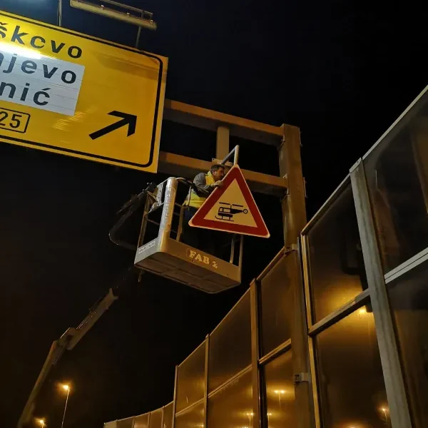 Djelatnik u auto-košari postavlja prometni znak opasnosti na portal tijekom noćnih radova