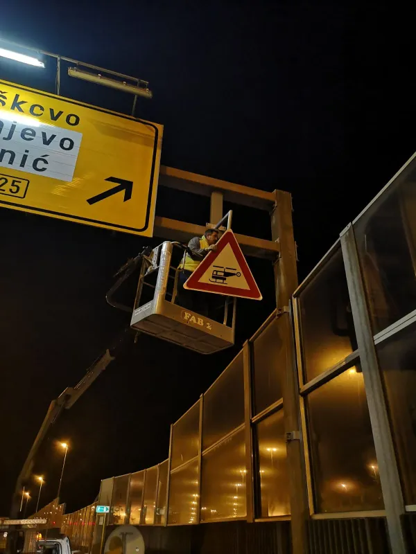 Djelatnik u auto-košari postavlja prometni znak opasnosti na portal tijekom noćnih radova