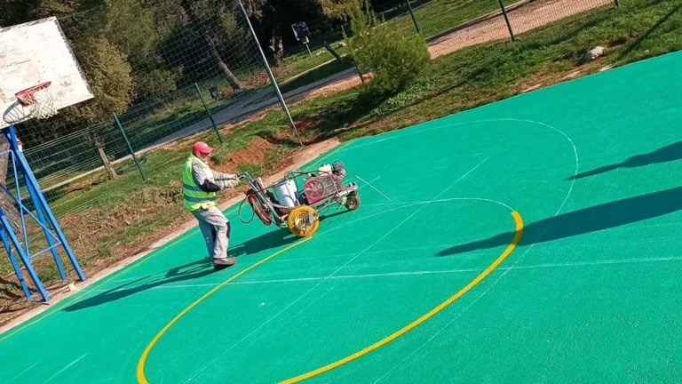 Radnik u zaštitnoj opremi nanosi boju na sportsko igralište.