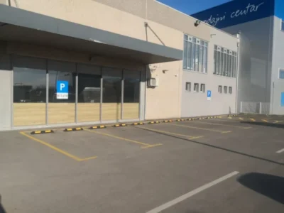 Niz postavljenih parkirnih graničnika unutar iscrtanih žutih parkirnih mjesta ispred prodajnog centra.