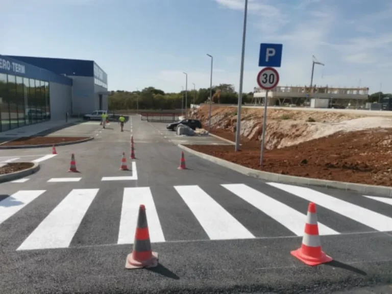 Široki prikaz uređenog parkirališta s pješačkim prijelazima i vertikalnom signalizacijom.