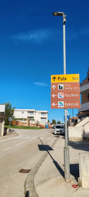 Putokazne ploče na stupu javne rasvjete s usmjerenjima za Pulu, plažu i Kamenjak