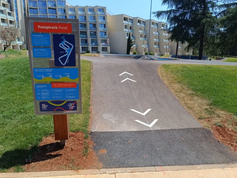 Asfaltirana pumptrack staza s plavim rubnim linijama i bijelim strelicama za smjer vožnje.