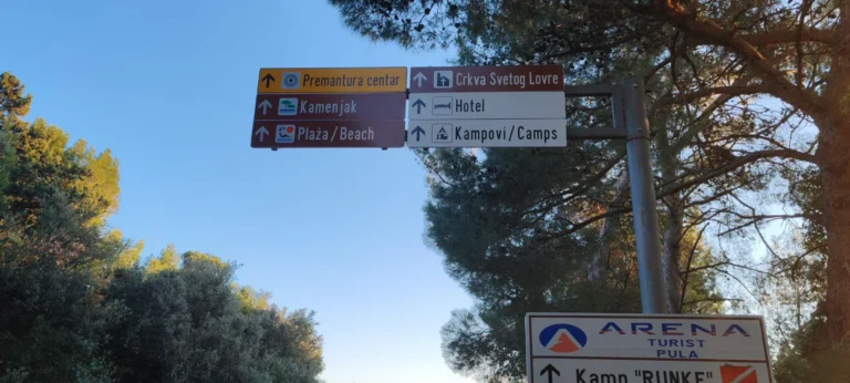 Niz turističkih znakova postavljenih na metalni stup u borovoj šumi