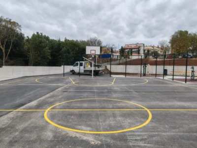 Široki kadar sportskog terena u Puli sa zelenom zaštitnom ogradom i parkiranim radnim vozilom u pozadini.