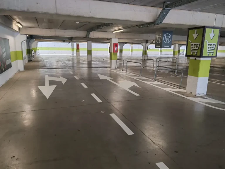 Jasne bijele strelice na podu garaže koje vozače usmjeravaju prema izlazu i blagajnama.