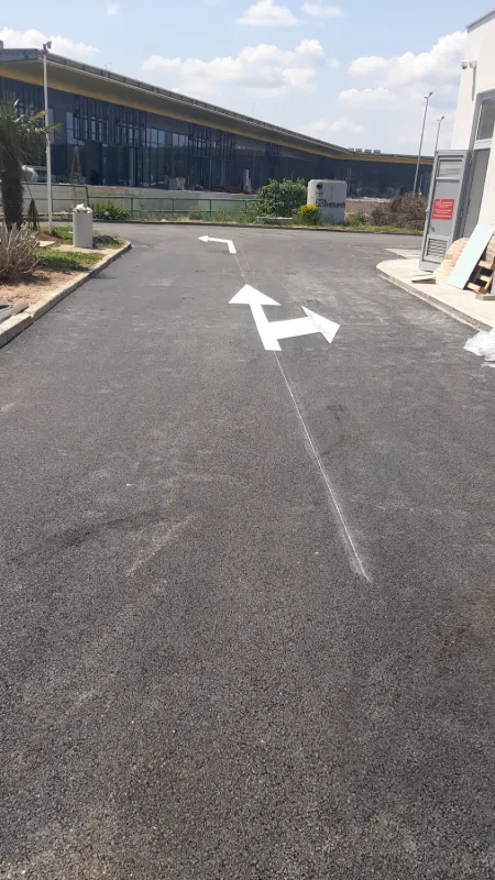 Velike bijele strelice za regulaciju smjera kretanja vozila na asfaltu ispred objekta.