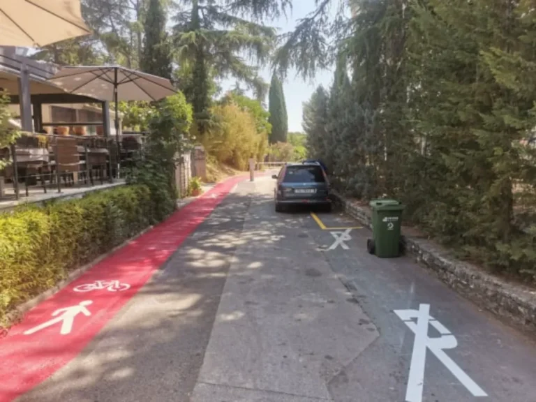 Biciklistička i pješačka staza crvene boje koja prolazi kroz turistički kompleks uz parkirana vozila