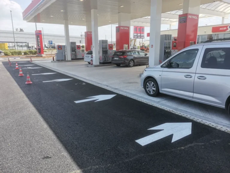 Bijele usmjerne strelice iscrtane na asfaltu koje vode vozila prema točionicima goriva.