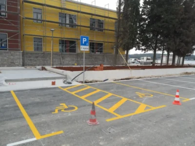 ProstranŽutom bojom označena parkirna mjesta za osobe s invaliditetom uz vertikalni prometni znako parkiralište s jasno iscrtanim bijelim linijama i prometnim znakovima