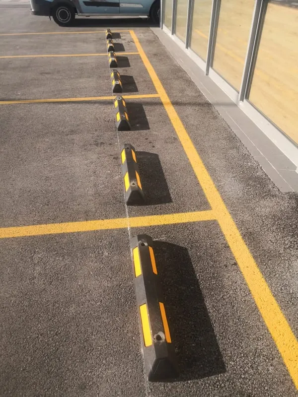 Detaljan prikaz gumenog parkirnog graničnika s reflektirajućim žutim trakama na parkiralištu.