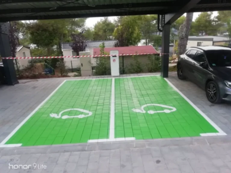 Dva zeleno obojana parkirna mjesta s bijelim simbolima za punjenje električnih automobila