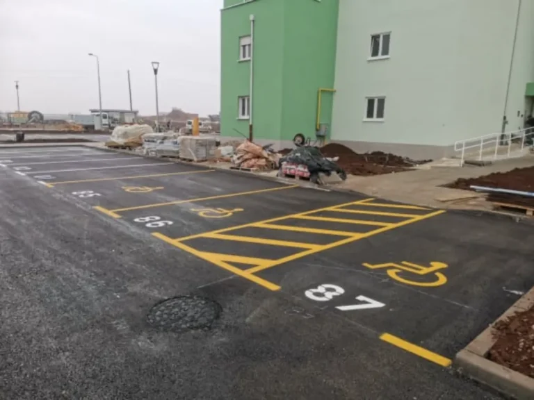 Žuta horizontalna signalizacija s kosim linijama za invalidska parkirališna mjesta ispred zgrade.
