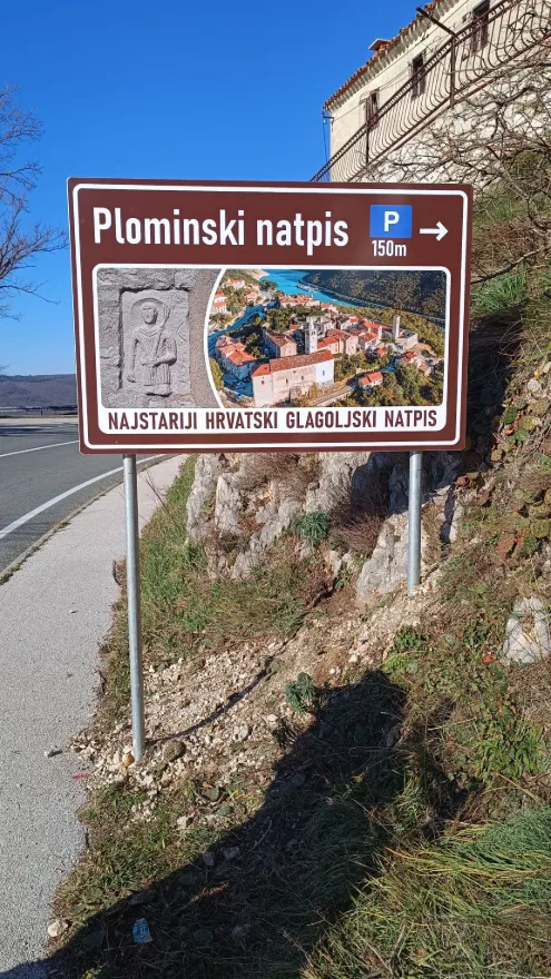 Informativna ploča za najstariji hrvatski glagoljski natpis postavljena na dvostruke stupove u Plominu.