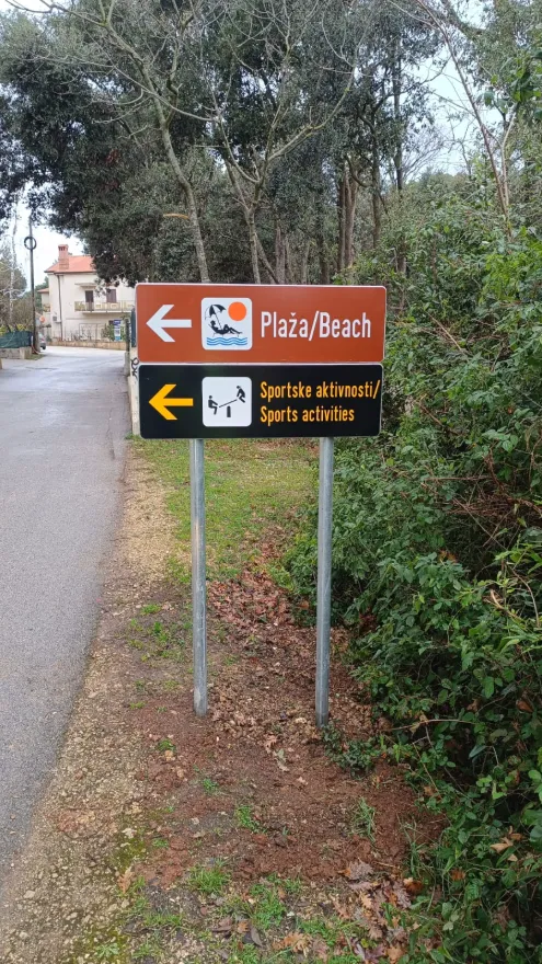 Smeđa i crna putokazna ploča za plažu i sportske aktivnosti u Banjolama.
