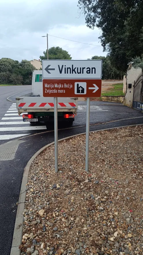 Smeđi turistički putokaz koji usmjerava posjetitelje prema Vinkuranu i lokalnoj crkvi.