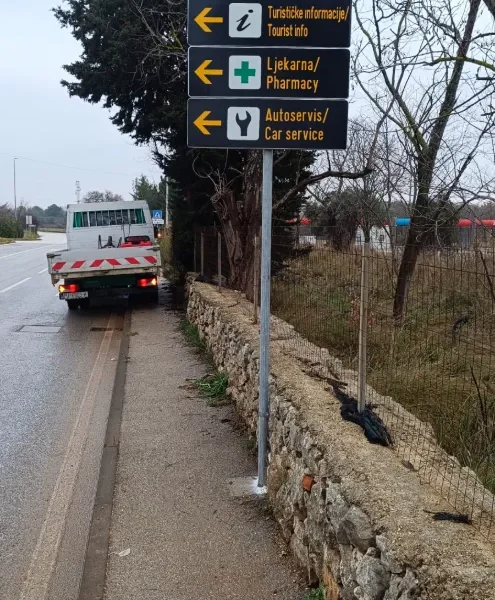 Postavljeni crni putokazi za turističke informacije, ljekarnu i autoservis u Banjolama na pocinčanom stupu.