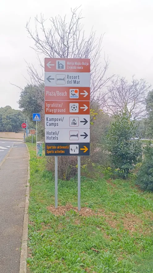 Detaljan prikaz vertikalne signalizacije uz cestu koja usmjerava prema lokalnim plažama i crkvi.