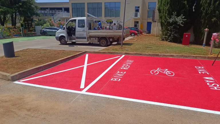 Crveno obojana asfaltna površina s bijelim natpisima BIKE REPAIR i BIKE WASH kod Hotela Parentino