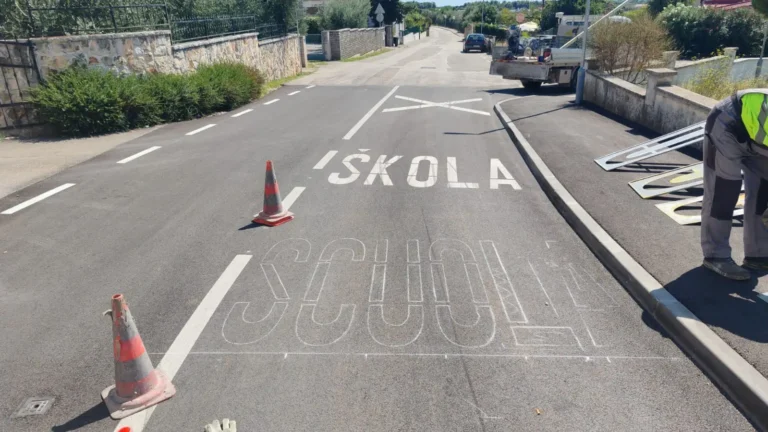 Radnici tvrtke Ličilac d.o.o. koriste šablone za iscrtavanje dvojezičnog natpisa scuola na cesti.