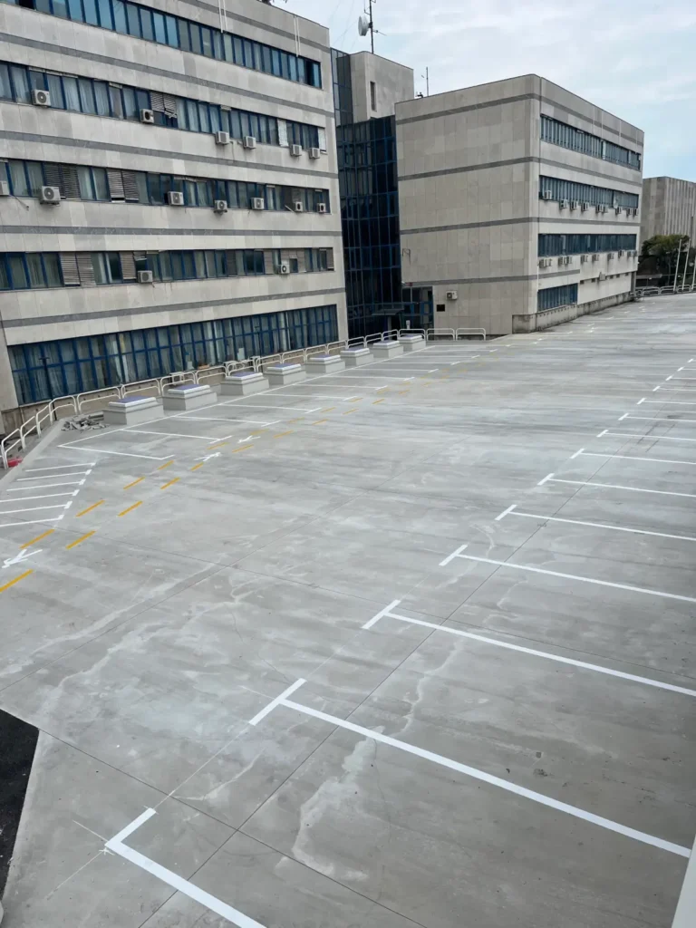 Široki prikaz betonskog platoa s precizno izvučenim bijelim parkirnim linijama i žutim pješačkim oznakama