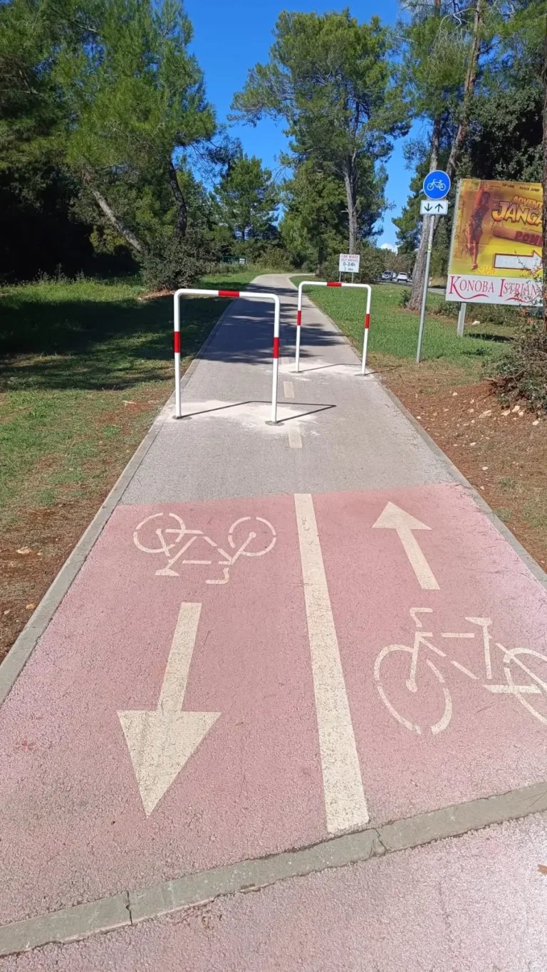 Pocinčane barijere s reflektirajućim trakama na crveno označenoj biciklističkoj stazi u blizini šume.